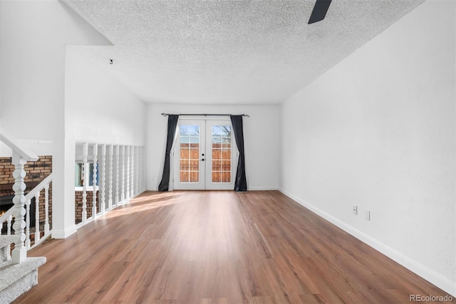 spare room featuring french doors, a textured ceiling, wood finished floors, baseboards, and stairs