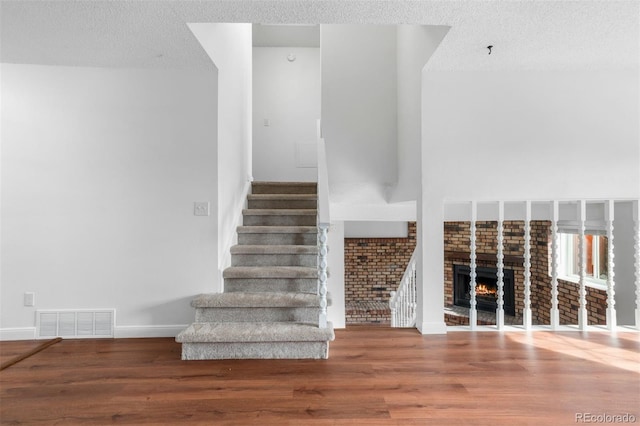 staircase with a fireplace, visible vents, a textured ceiling, wood finished floors, and baseboards