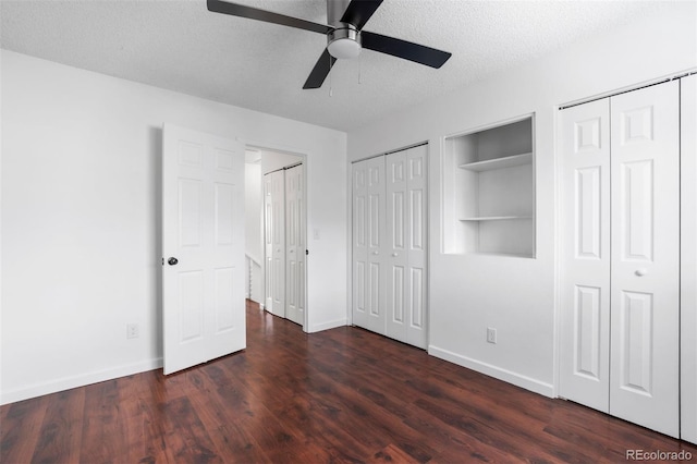 unfurnished bedroom featuring a textured ceiling, ceiling fan, dark wood-type flooring, baseboards, and multiple closets