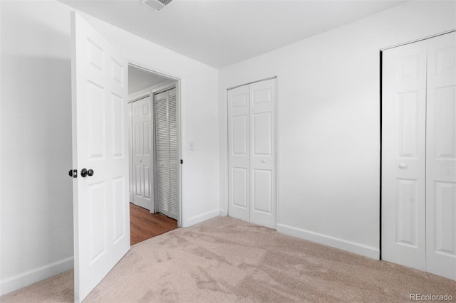 unfurnished bedroom with two closets, baseboards, and carpet flooring