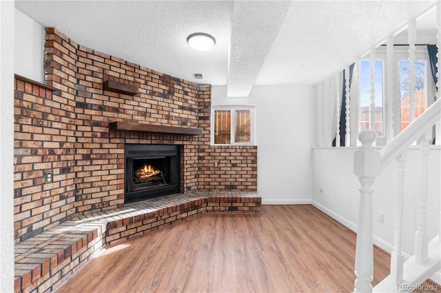 unfurnished living room featuring a brick fireplace, a textured ceiling, wood finished floors, baseboards, and stairs