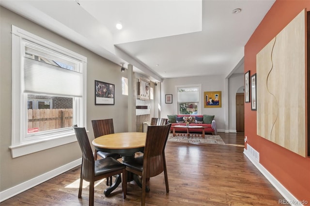 dining area with arched walkways, visible vents, baseboards, and dark wood finished floors