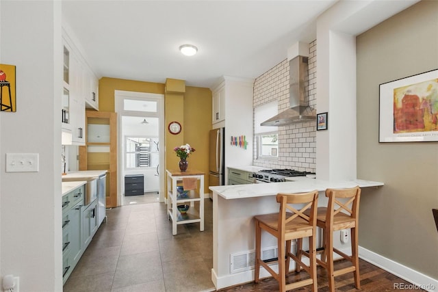kitchen with wall chimney exhaust hood, light countertops, freestanding refrigerator, range with gas stovetop, and backsplash