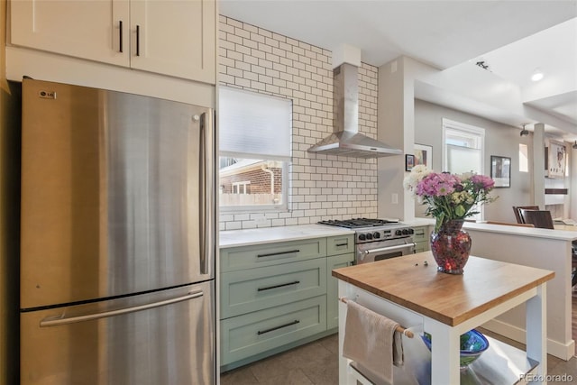 kitchen featuring tasteful backsplash, butcher block counters, wall chimney range hood, stainless steel appliances, and green cabinetry