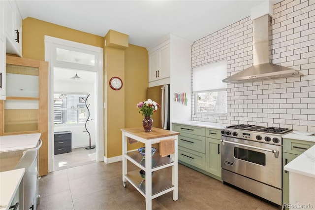 kitchen with tasteful backsplash, wall chimney range hood, white cabinets, appliances with stainless steel finishes, and green cabinetry