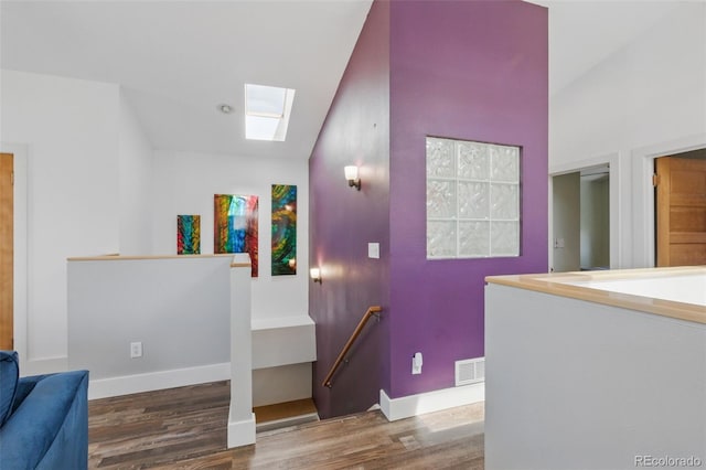 interior space featuring lofted ceiling with skylight, visible vents, baseboards, and wood finished floors