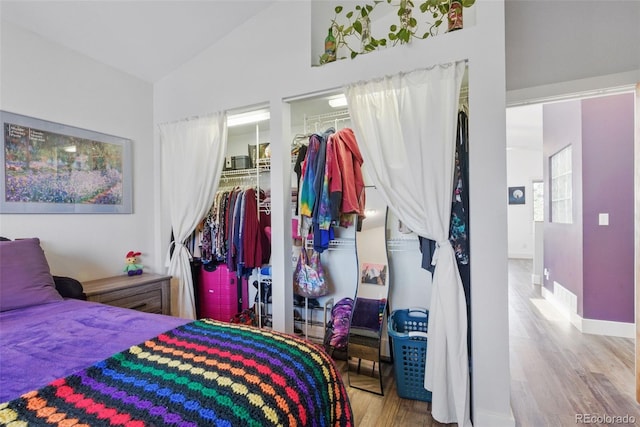 bedroom featuring baseboards, a closet, vaulted ceiling, a walk in closet, and wood finished floors