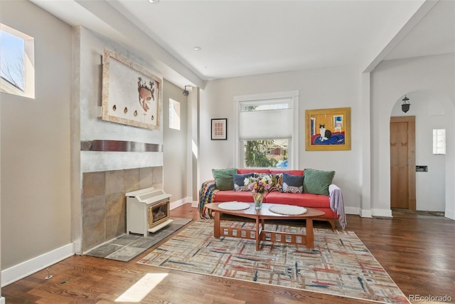 sitting room featuring arched walkways, a wood stove, baseboards, and wood finished floors