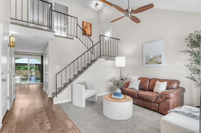living area featuring a high ceiling, wood finished floors, stairs, a ceiling fan, and baseboards