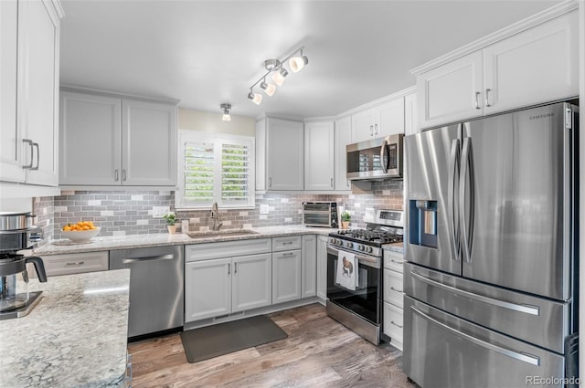 kitchen featuring stainless steel appliances, a sink, tasteful backsplash, white cabinetry, and light wood finished floors