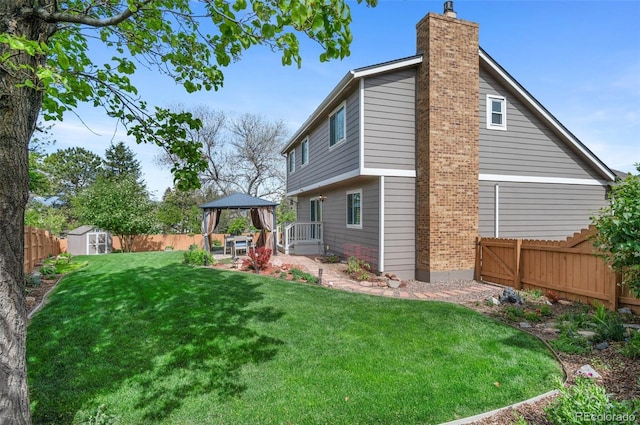 back of house featuring a gazebo, a chimney, a shed, a patio, and an outbuilding