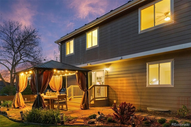 back of house at dusk featuring a gazebo and fence