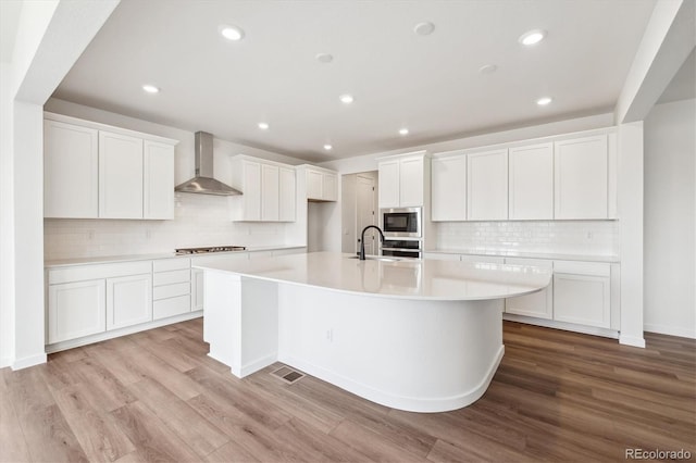 24748 E 40th Ave, Aurora, CO 80019 - kitchen with wall chimney range hood, appliances with stainless steel finishes, a large island, tasteful backsplash, and light wood-style floors