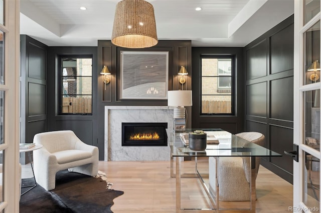 interior space with light wood-style floors, a glass covered fireplace, a raised ceiling, and a decorative wall