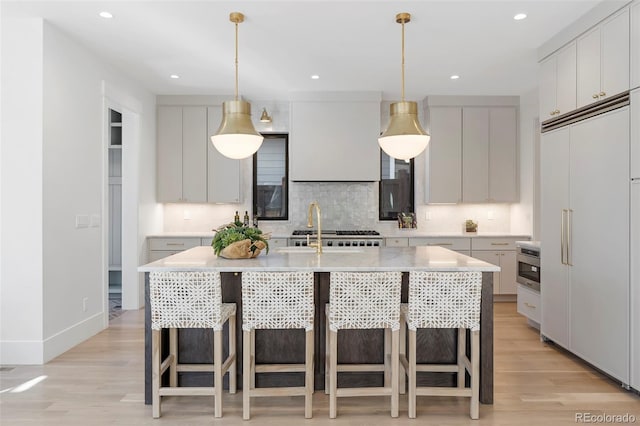 kitchen with an island with sink, paneled built in refrigerator, light countertops, and a sink