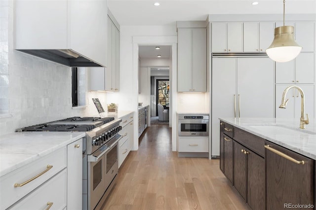 kitchen featuring stainless steel appliances, a sink, white cabinetry, dark brown cabinets, and light wood finished floors