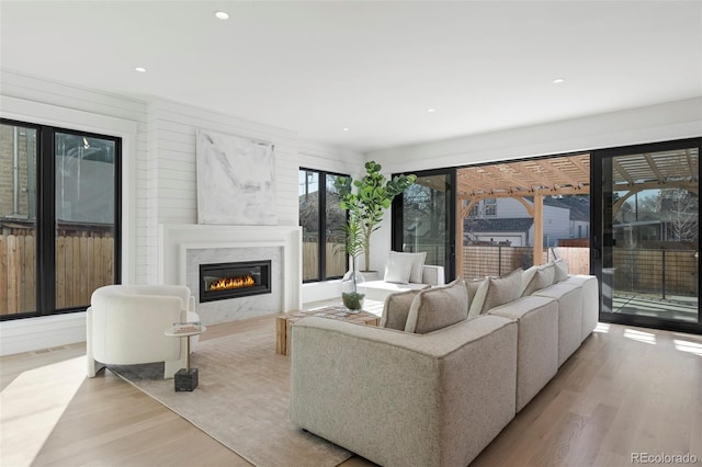 living room featuring recessed lighting, light wood-style flooring, visible vents, and a glass covered fireplace