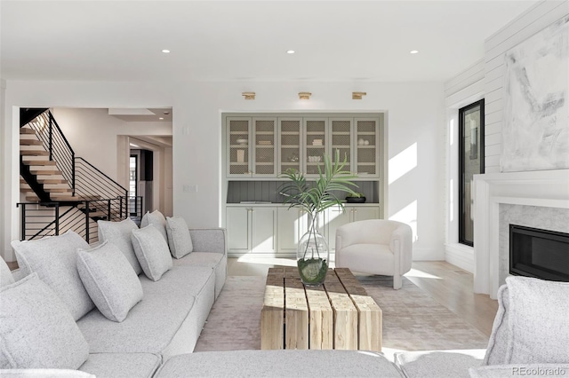 living room featuring a glass covered fireplace, stairway, light wood finished floors, and recessed lighting