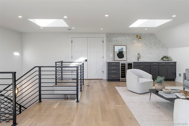 interior space with light wood-style floors, recessed lighting, beverage cooler, and an upstairs landing