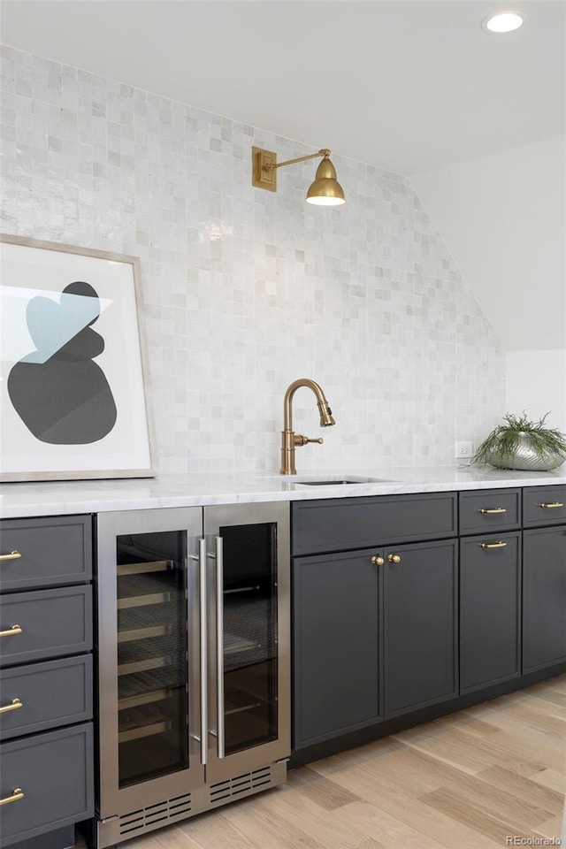 bar featuring light wood-style flooring, beverage cooler, a sink, vaulted ceiling, and decorative backsplash