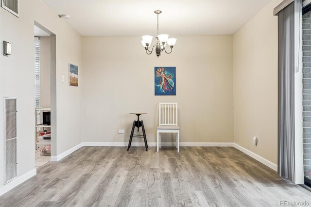 spare room featuring wood finished floors, a chandelier, and baseboards