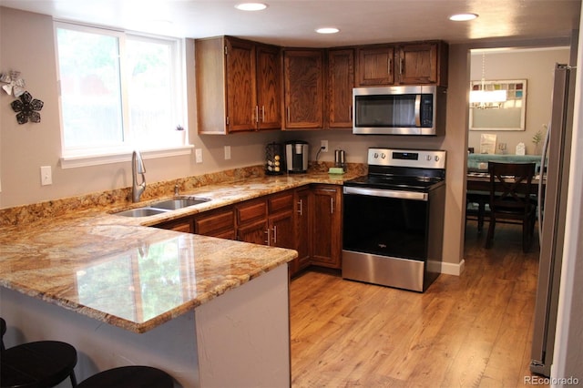7394 S Field Ct, Littleton, CO 80128 - kitchen with stainless steel appliances, a peninsula, light stone counters, light wood-style flooring, and a breakfast bar