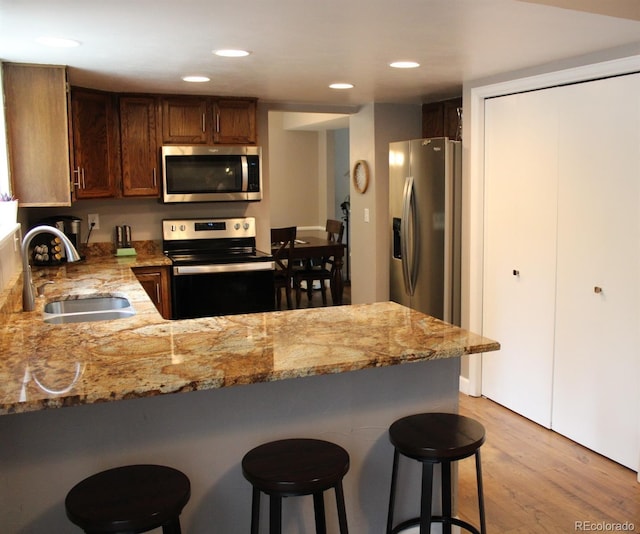 7394 S Field Ct, Littleton, CO 80128 - kitchen with stainless steel appliances, a peninsula, light wood-style floors, a breakfast bar, and light stone countertops