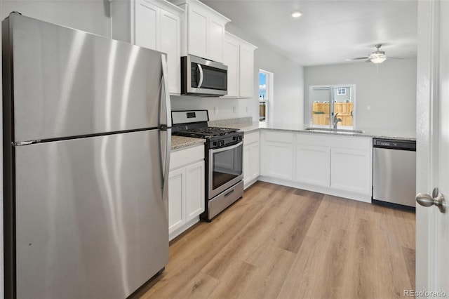 kitchen featuring light wood finished floors, light stone counters, stainless steel appliances, white cabinetry, and a sink