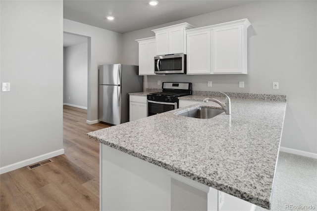 kitchen with sink, kitchen peninsula, white cabinetry, stainless steel appliances, and light hardwood / wood-style flooring