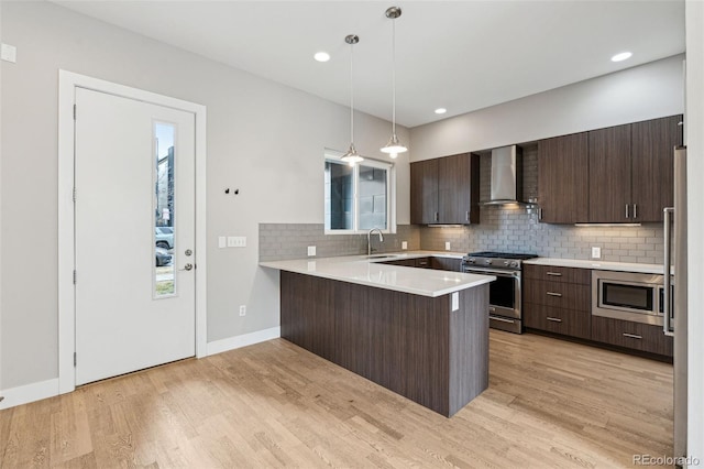 kitchen with kitchen peninsula, decorative light fixtures, sink, appliances with stainless steel finishes, and wall chimney range hood