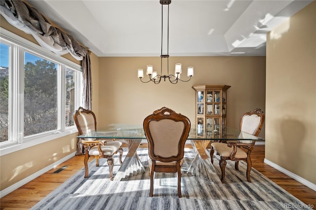 dining area featuring a notable chandelier, wood-type flooring, and a raised ceiling