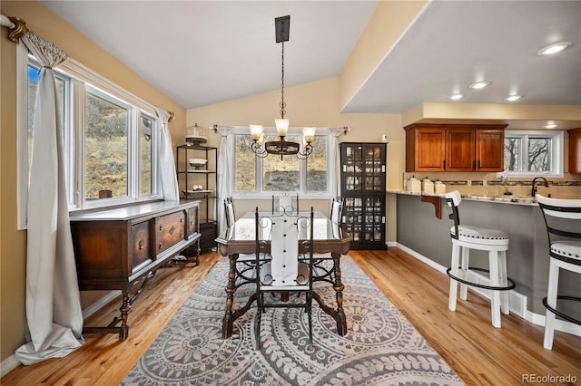 dining room with sink, vaulted ceiling, light hardwood / wood-style floors, and a chandelier