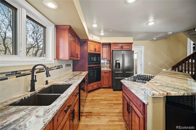 kitchen featuring tasteful backsplash, sink, light stone counters, black appliances, and light hardwood / wood-style flooring