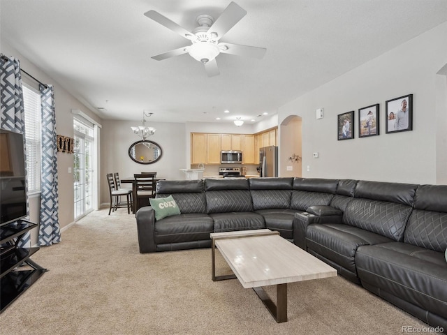 carpeted living room with ceiling fan with notable chandelier