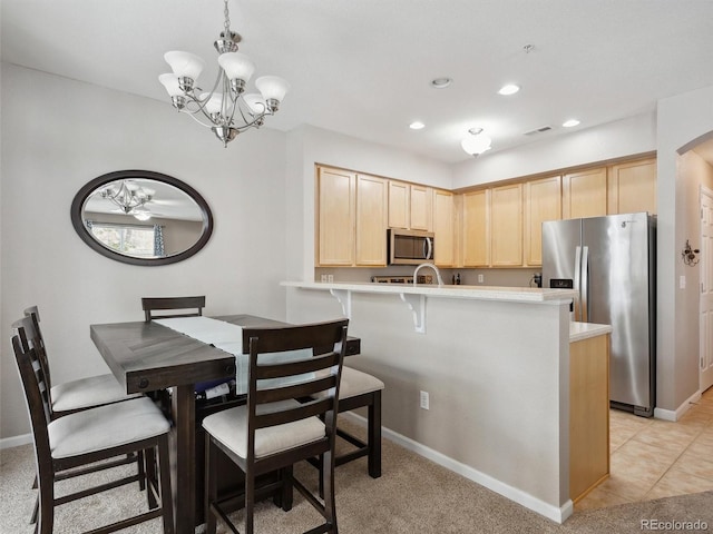 kitchen featuring kitchen peninsula, light brown cabinetry, stainless steel appliances, and a notable chandelier