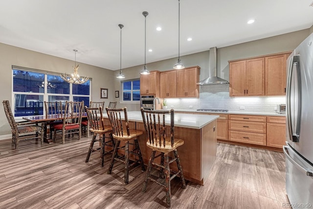 788 Alumroot St, Castle Rock, CO 80104 - kitchen featuring wall chimney exhaust hood, appliances with stainless steel finishes, wood finished floors, light countertops, and decorative backsplash