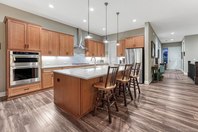 788 Alumroot St, Castle Rock, CO 80104 - kitchen with wall chimney exhaust hood, appliances with stainless steel finishes, a sink, wood finished floors, and a kitchen island with sink