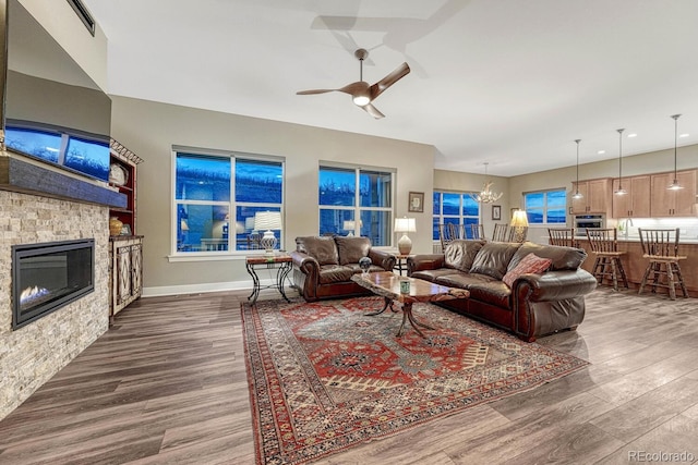 788 Alumroot St, Castle Rock, CO 80104 - living room featuring dark wood finished floors, ceiling fan, a stone fireplace, a chandelier, and baseboards