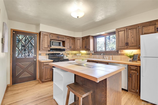 kitchen featuring sink, a center island, tile counters, stainless steel appliances, and light hardwood / wood-style flooring