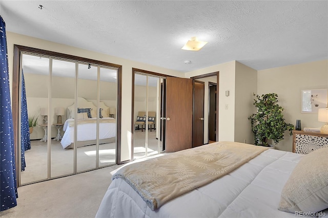 bedroom featuring light colored carpet, a textured ceiling, and two closets