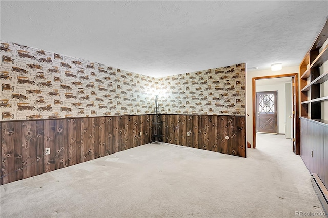 carpeted empty room with a baseboard radiator, a textured ceiling, and wood walls