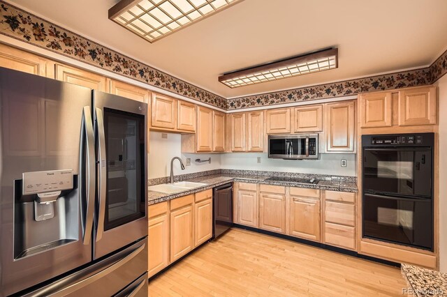 kitchen with light brown cabinets, black appliances, light wood-type flooring, and a sink