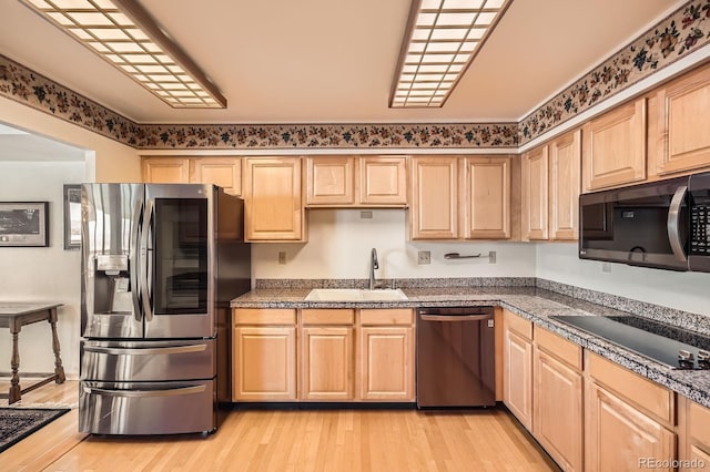 kitchen featuring light brown cabinetry, a sink, stainless steel appliances, light wood-style floors, and tile counters