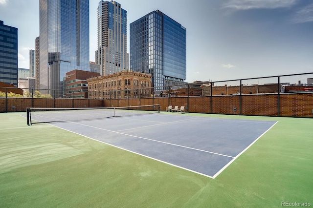 view of tennis court with a view of city and fence