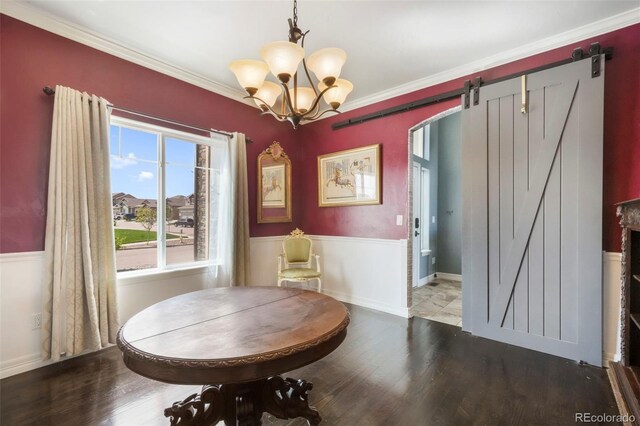 10525 Mt Sherman Way, Peyton, CO 80831 - dining room with a barn door, wood finished floors, a chandelier, a wainscoted wall, and crown molding