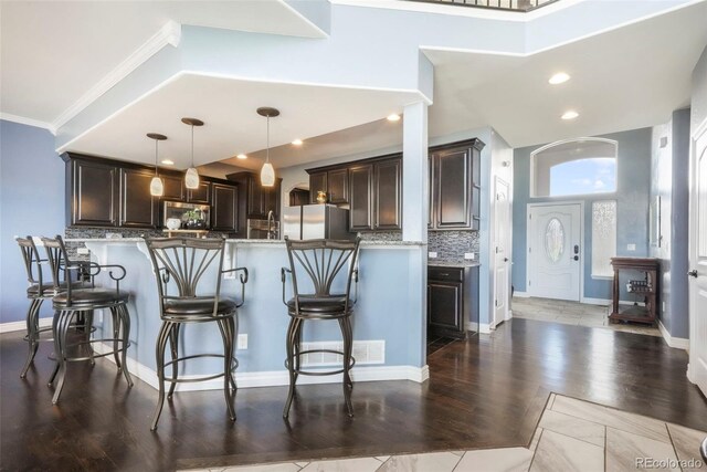 10525 Mt Sherman Way, Peyton, CO 80831 - kitchen with dark brown cabinets, a breakfast bar, tasteful backsplash, decorative light fixtures, and crown molding