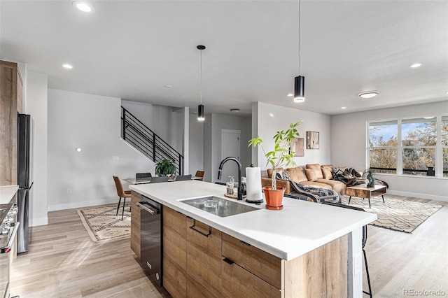 kitchen with an island with sink, hanging light fixtures, light hardwood / wood-style flooring, dishwashing machine, and sink