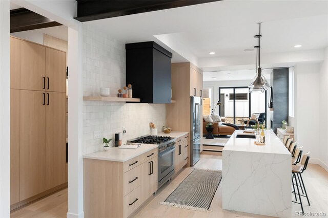 kitchen with pendant lighting, light hardwood / wood-style floors, a kitchen island with sink, tasteful backsplash, and stainless steel appliances