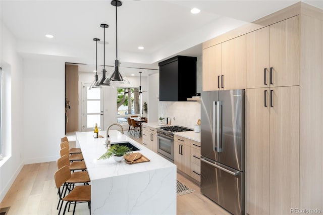 kitchen featuring light brown cabinets, sink, high end appliances, a center island with sink, and light wood-type flooring