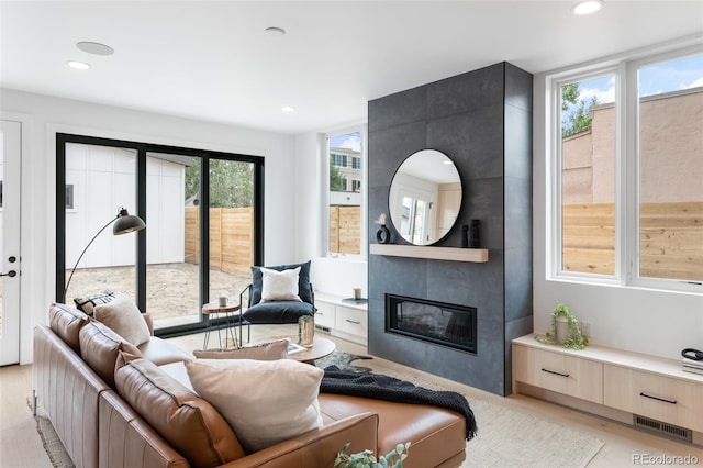 living area with light wood-type flooring, visible vents, a tiled fireplace, and recessed lighting